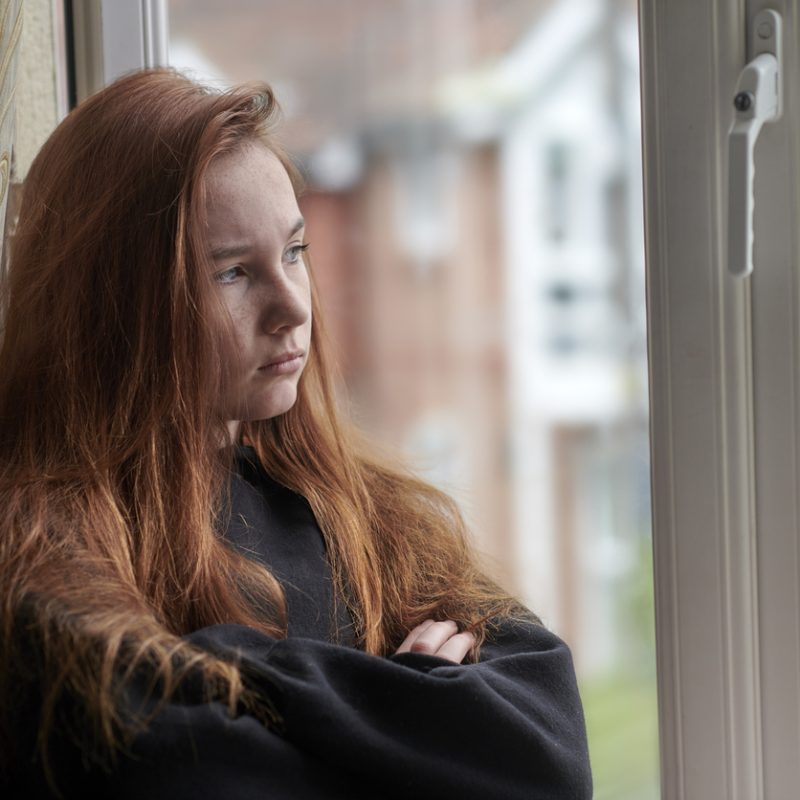 sad teen girl looking out window wondering how common is depression in teens?