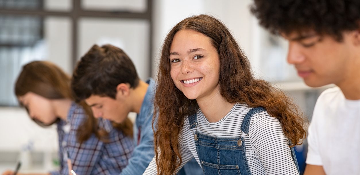 teen girl smiling in classroom after parents asked "what is a therapeutic day school?" and pursued admission